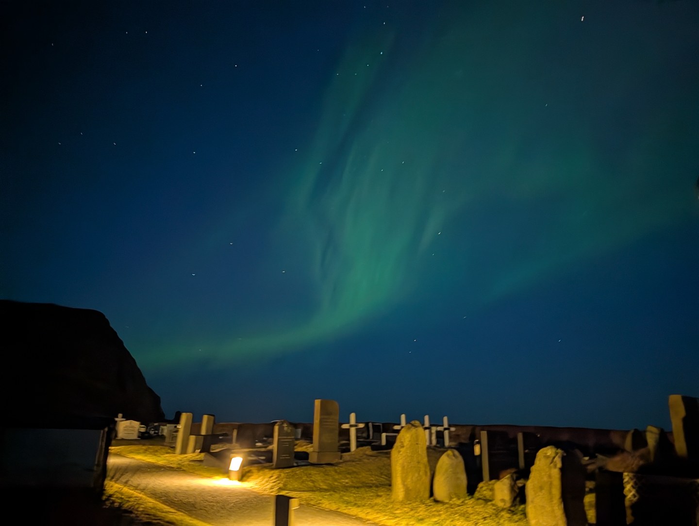 Green northern lights above gravestones and a nearby building