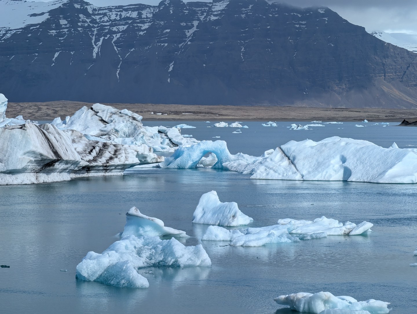 Blue-white icebergs floating in water beneath snowy mountains