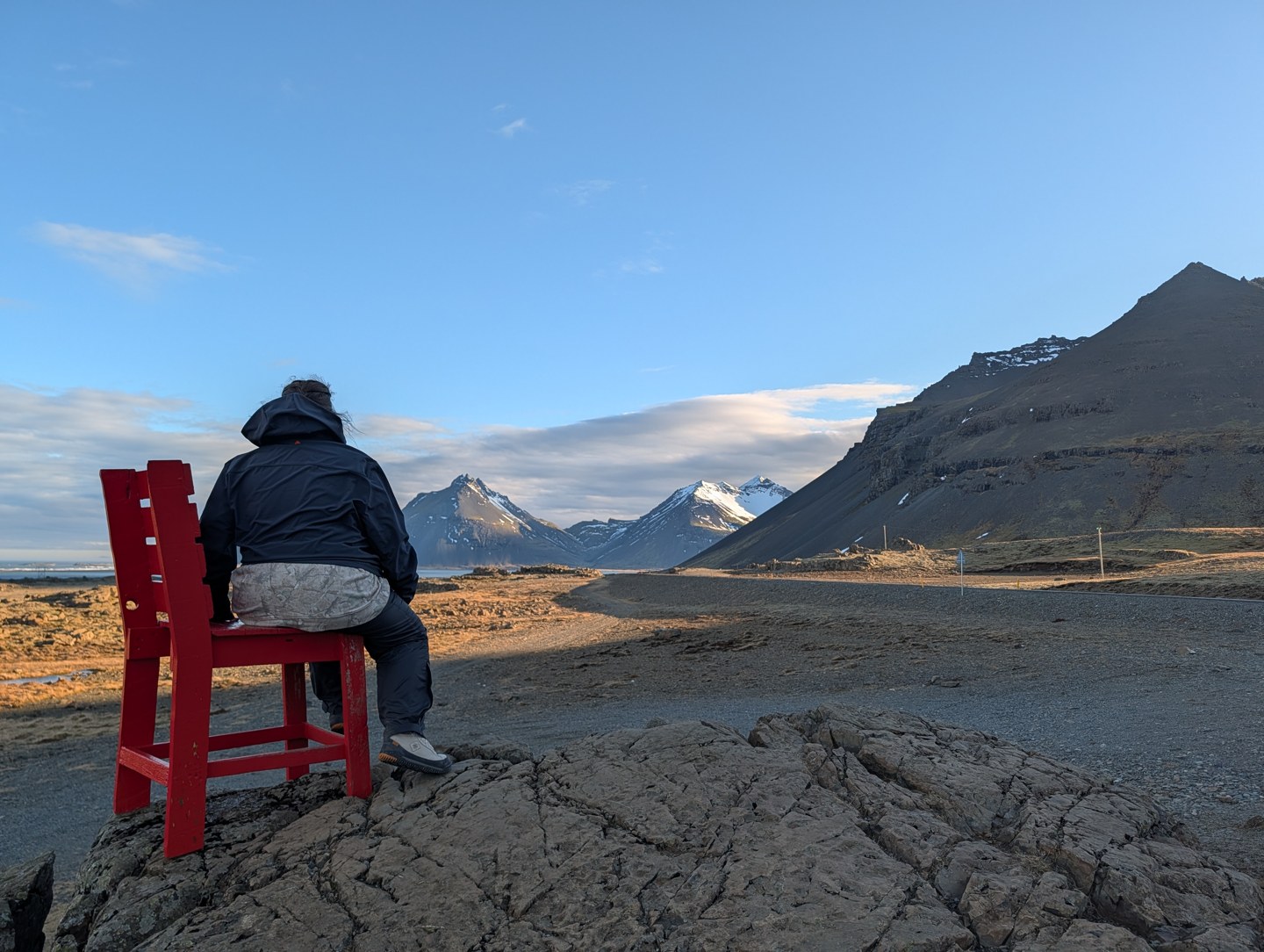 A seated traveler in a red chair facing a broad mountain landscape