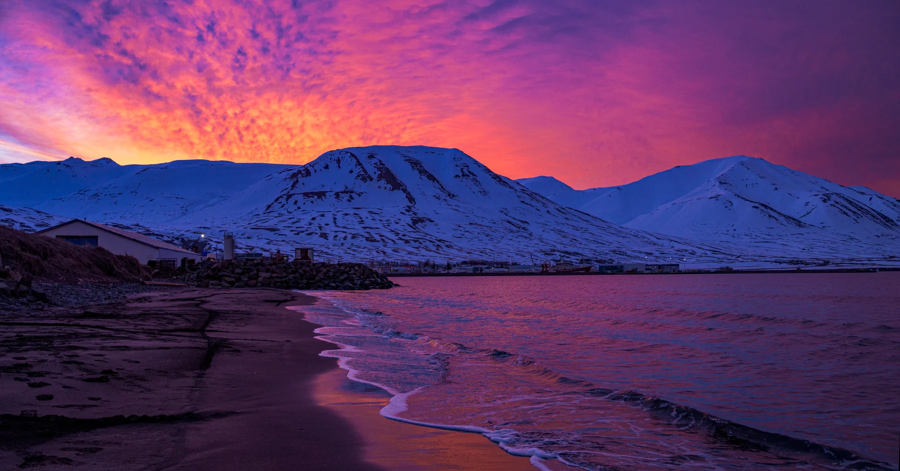Pink and orange sky above a shoreline and snow-covered mountains in Iceland
