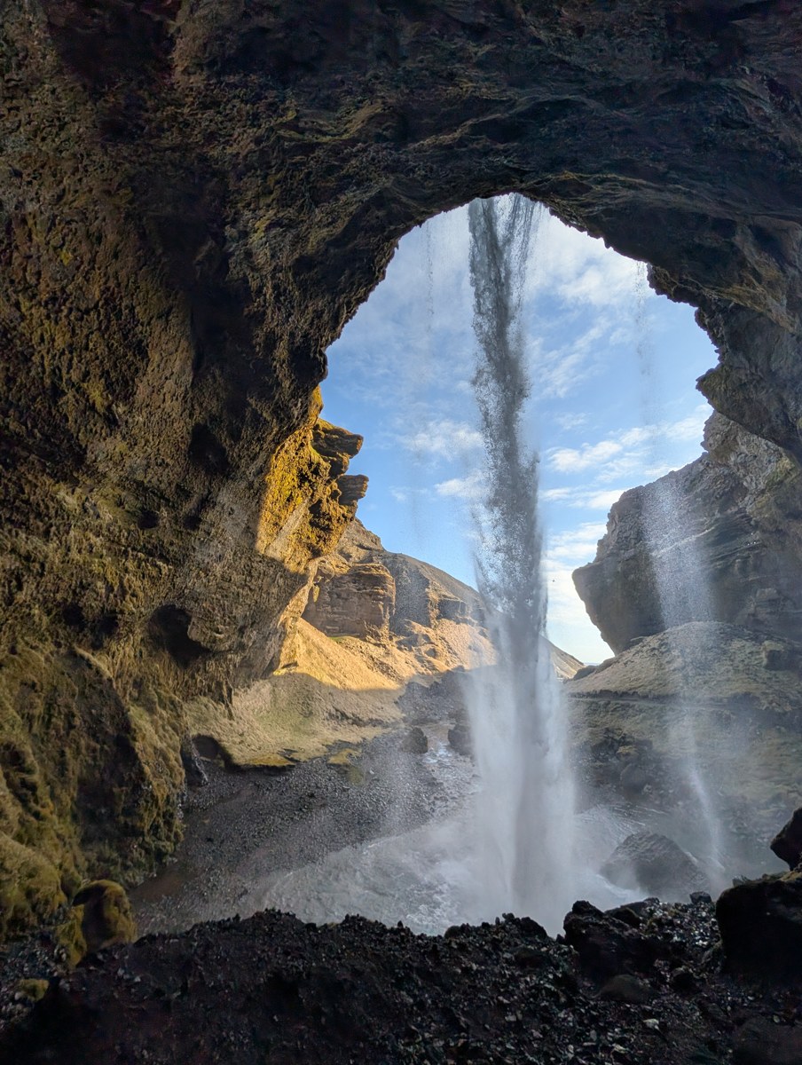 A waterfall viewed through a rounded opening in dark rock